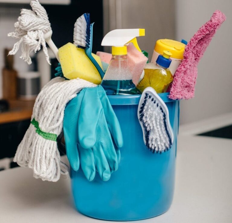 Cleaning products, detergents and chemicals in blue plastic bucket on kitchen worktop.