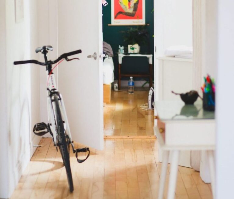 Clean, bright, light and airy hallway with wooden floors bicycle propped up against wall door to bedroom open.