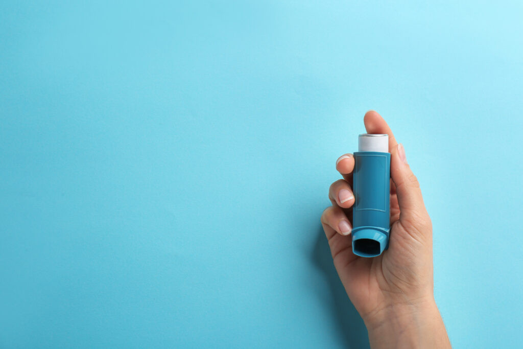 Woman holding blue inhaler for asthma on blue background