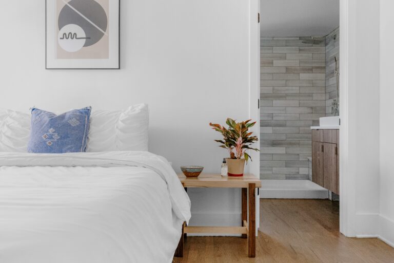 Bedroom with double bed white walls, white bed linen, wooden bedside table with plant, wooden floor and en suite.